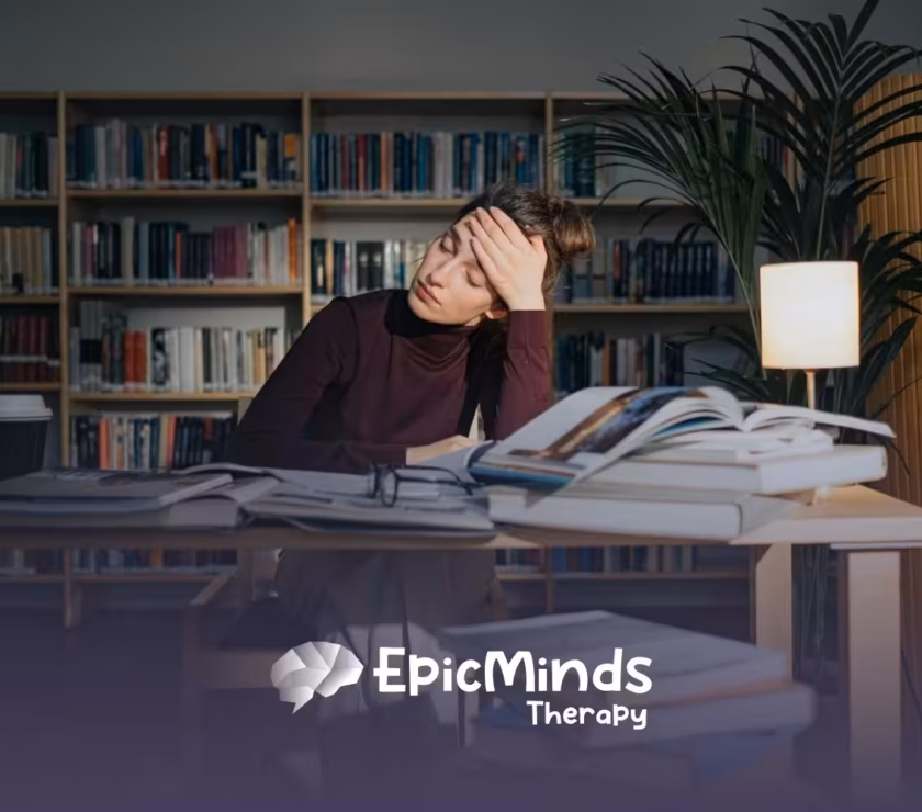 BCBA student in library looking tired while studying, surrounded by open books and a lamp in MD.