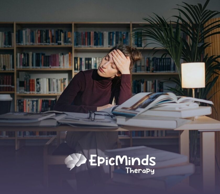 BCBA student in library looking tired while studying, surrounded by open books and a lamp in MD.
