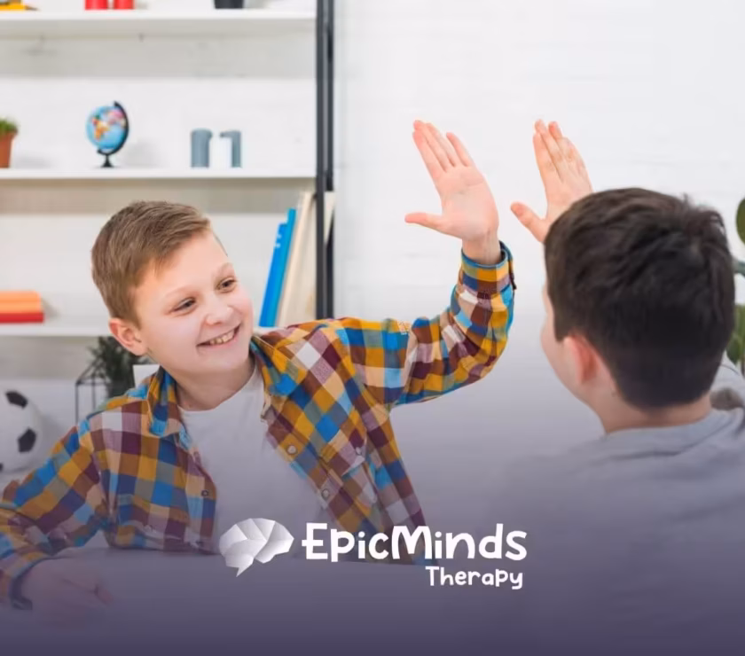 Two boys smiling and giving each other a high five while sitting at a table.