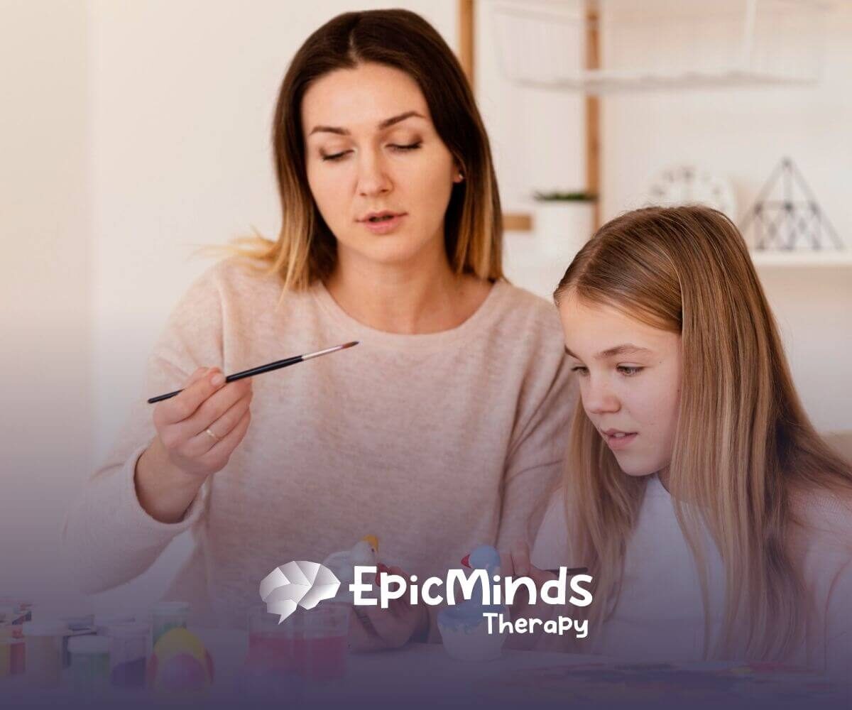 BCBA and autistic girl painting ceramic figures together at a table during ABA therapy.