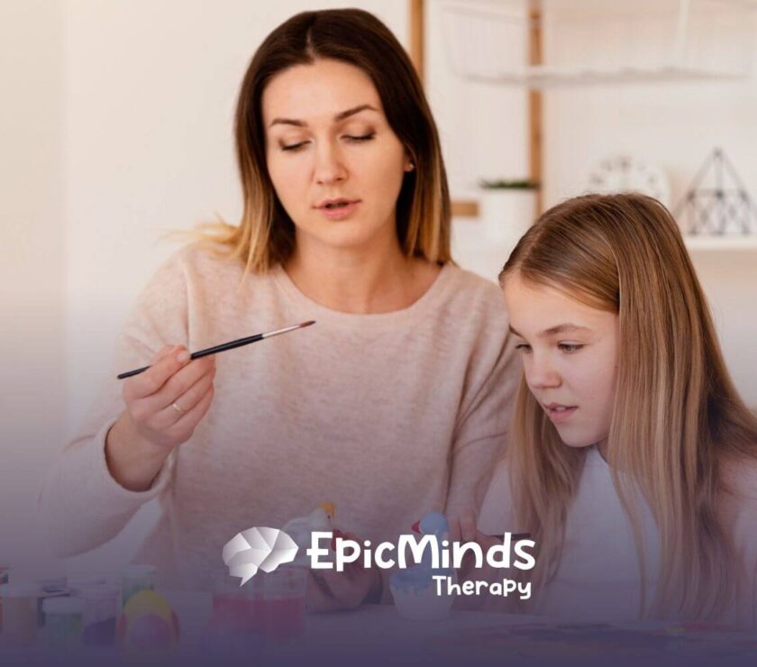 BCBA and autistic girl painting ceramic figures together at a table during ABA therapy.