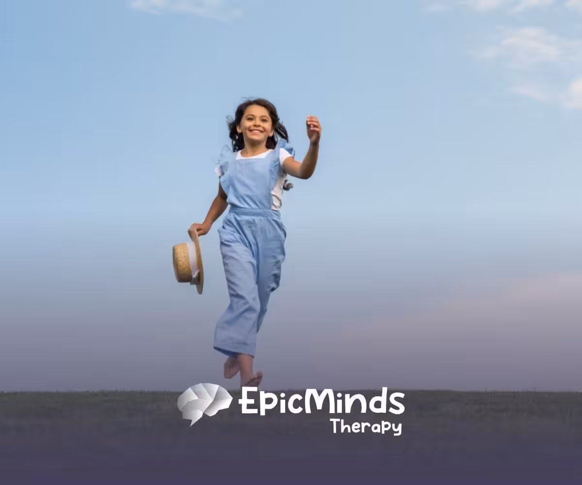 A young girl runs joyfully on a grassy field under a blue sky, holding a straw hat after ABA therapy.