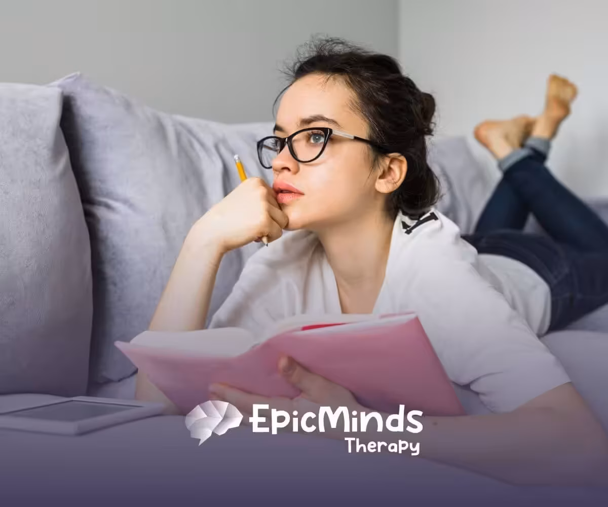 A young woman on the autism spectrum with glasses lies on a couch.