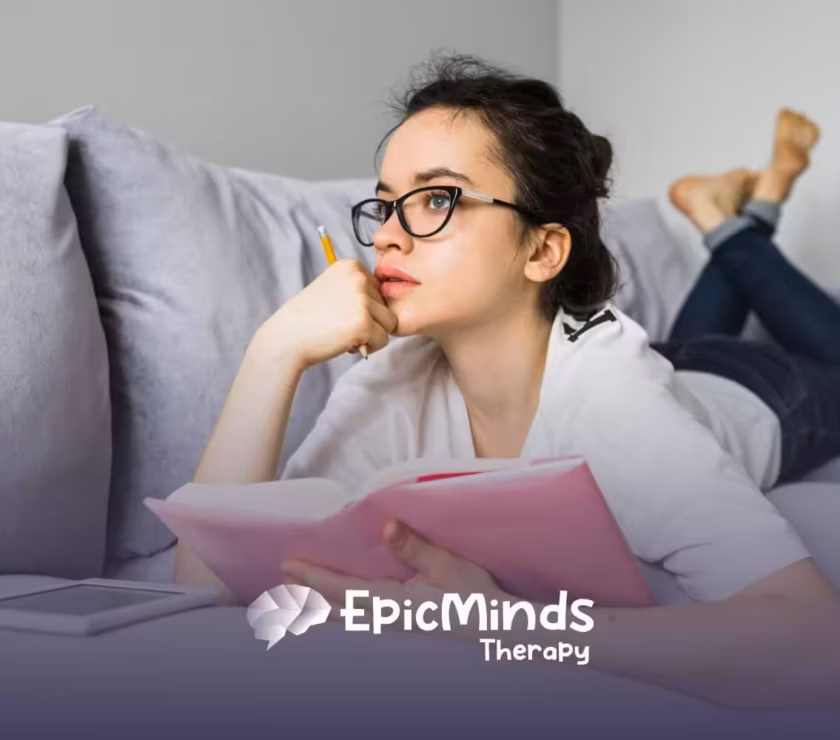 A young woman on the autism spectrum with glasses lies on a couch.