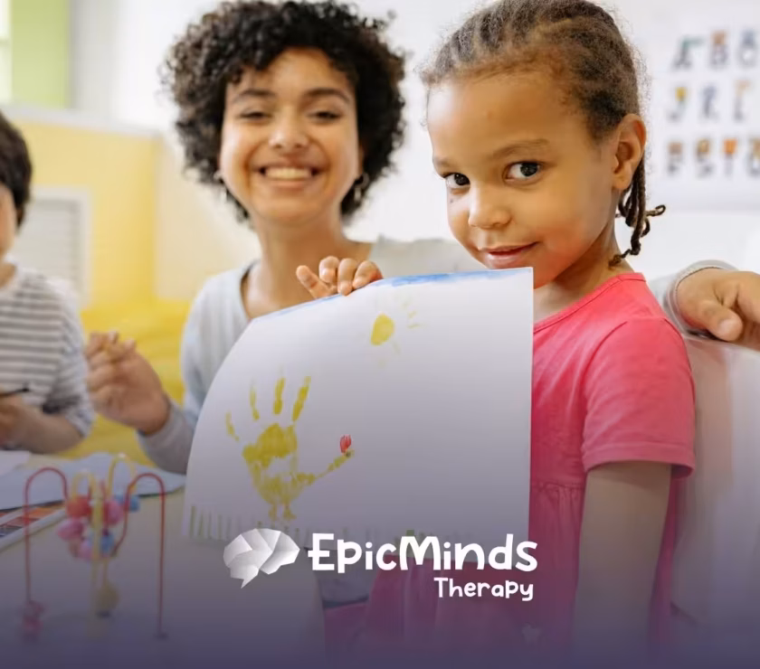 An autistic girl proudly showing her handprint artwork at a classroom during ABA therapy in NC.