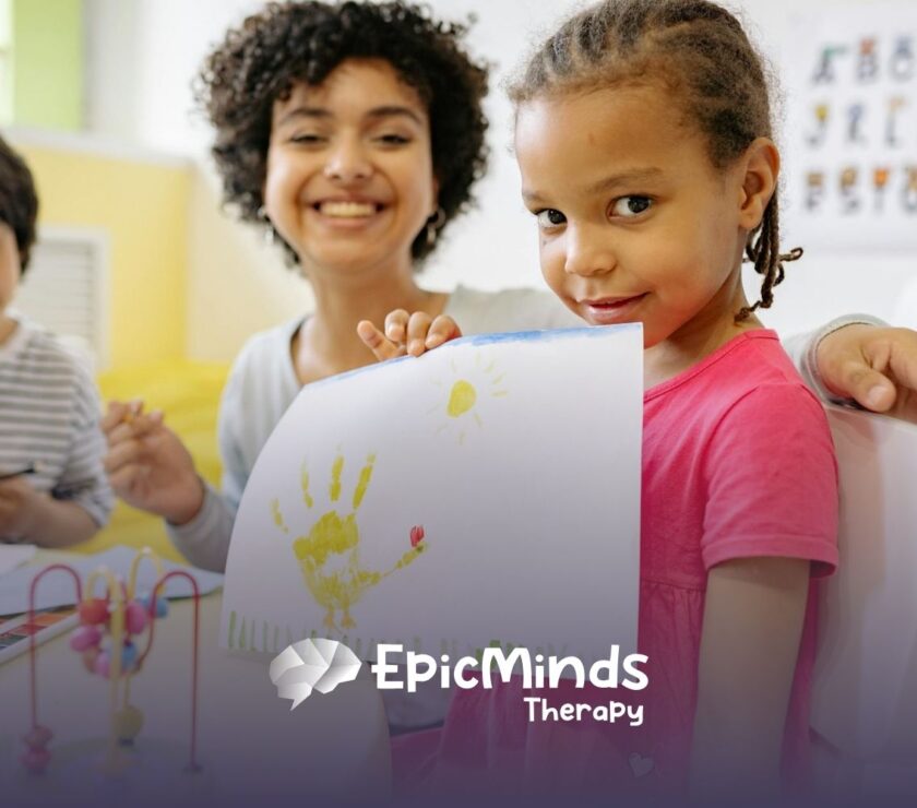 An autistic girl proudly showing her handprint artwork at a classroom during ABA therapy in NC.