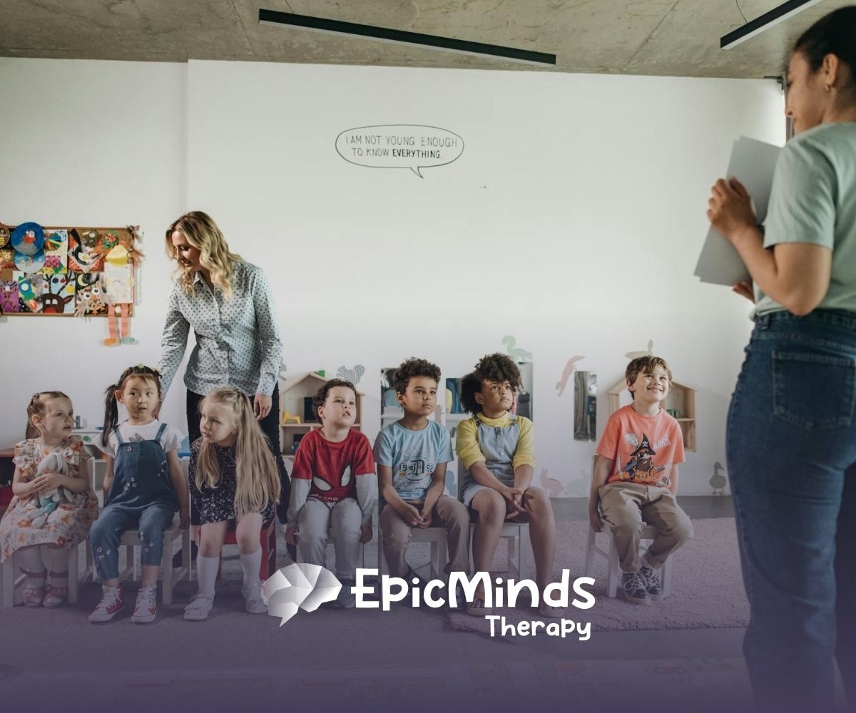 Group of autistic kids sitting in chairs during ABA therapy with an RBT and BCBA standing nearby.