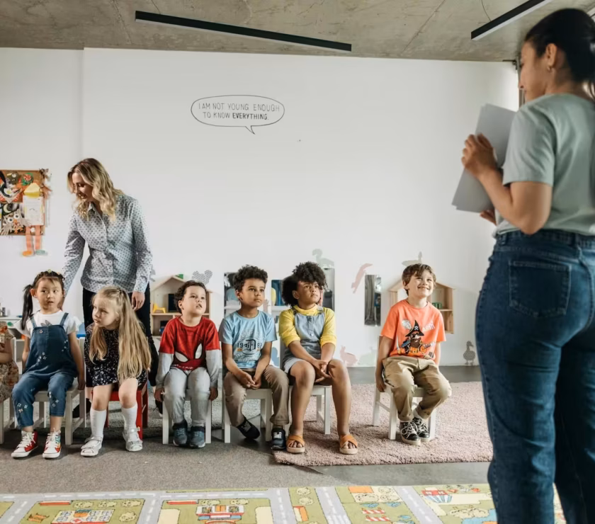 Group of autistic kids sitting in chairs during ABA therapy with an RBT and BCBA standing nearby.