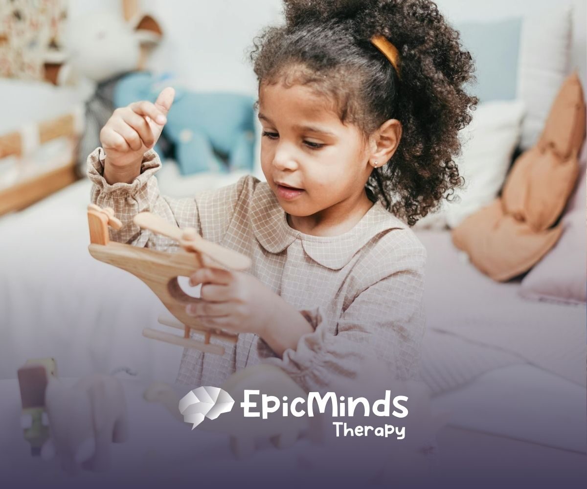 An autistic girl holding and inspecting a wooden toy helicopter at a table during ABA therapy in MD.