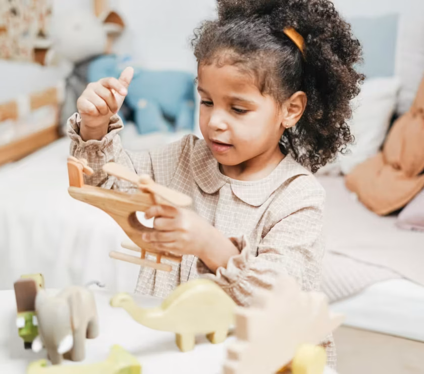 An autistic girl holding and inspecting a wooden toy helicopter at a table during ABA therapy in MD.