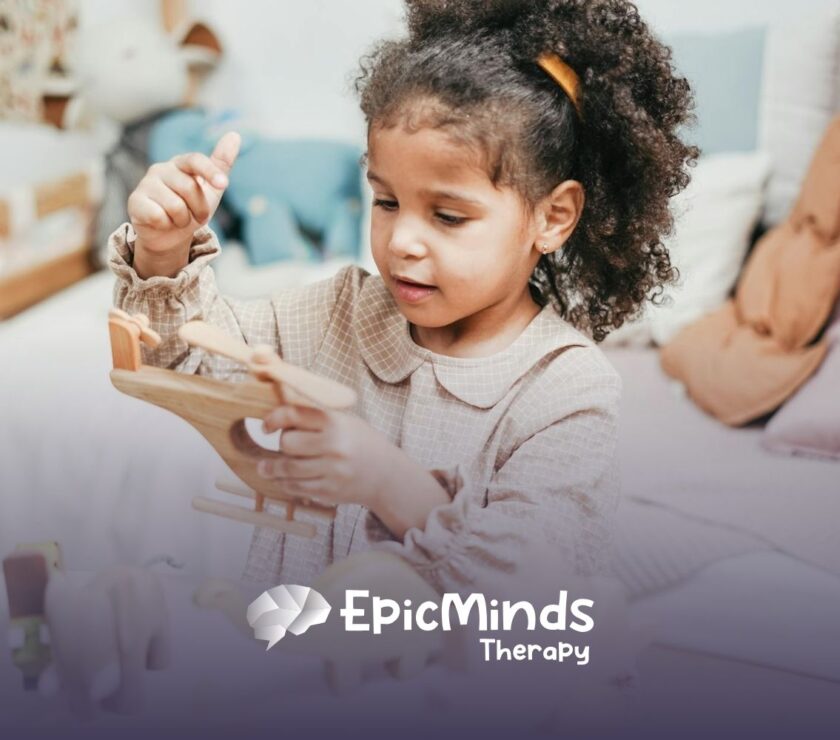 An autistic girl holding and inspecting a wooden toy helicopter at a table during ABA therapy in MD.
