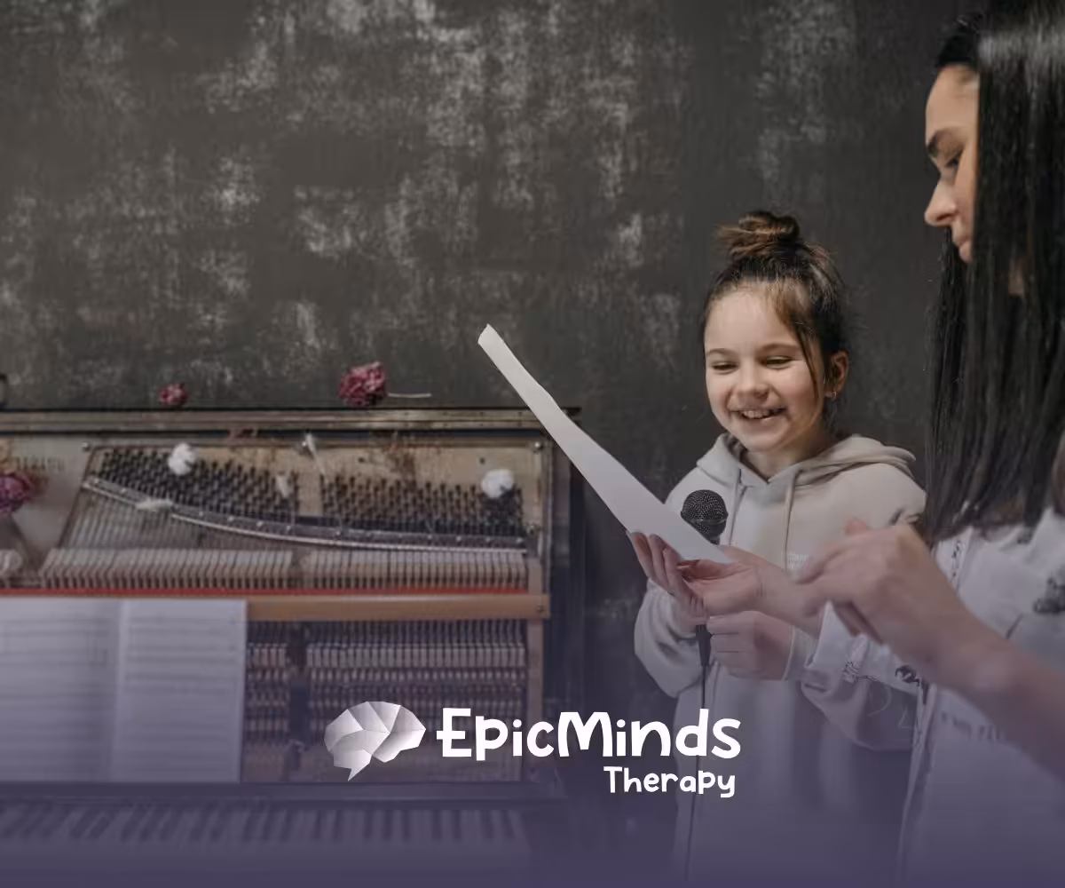 Young autistic girl smiling while reading a paper with an ABA therapist next to her at a piano during ABA therapy in NC.