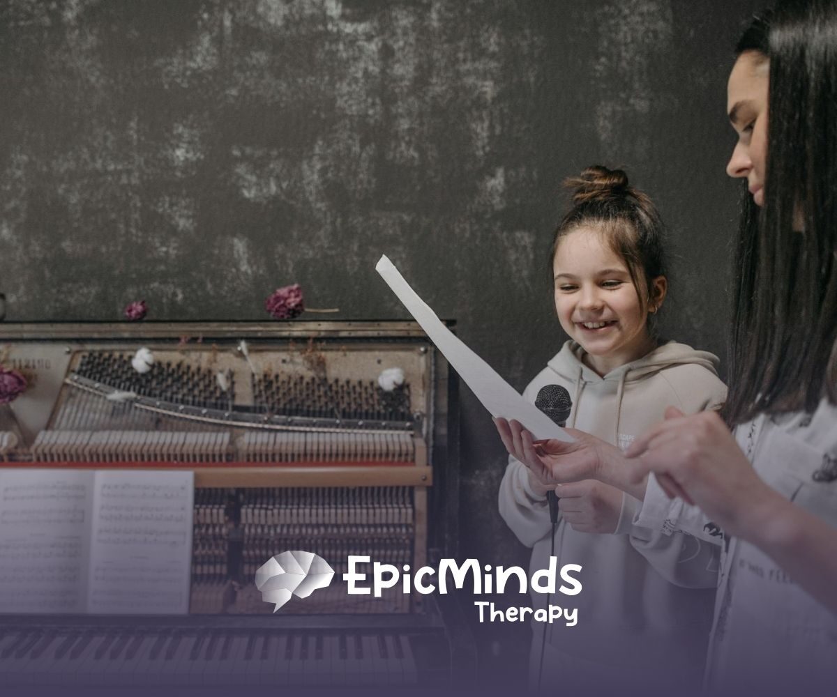 Young autistic girl smiling while reading a paper with an ABA therapist next to her at a piano during ABA therapy in NC.