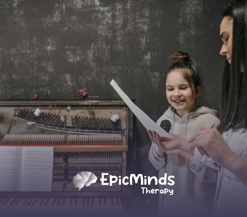 Young autistic girl smiling while reading a paper with an ABA therapist next to her at a piano during ABA therapy in NC.