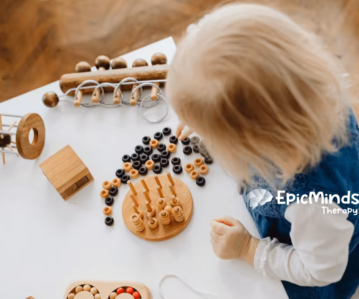 An autistic toddler playing with wooden Montessori toys on a white table during in-home ABA therapy in North Carolina.
