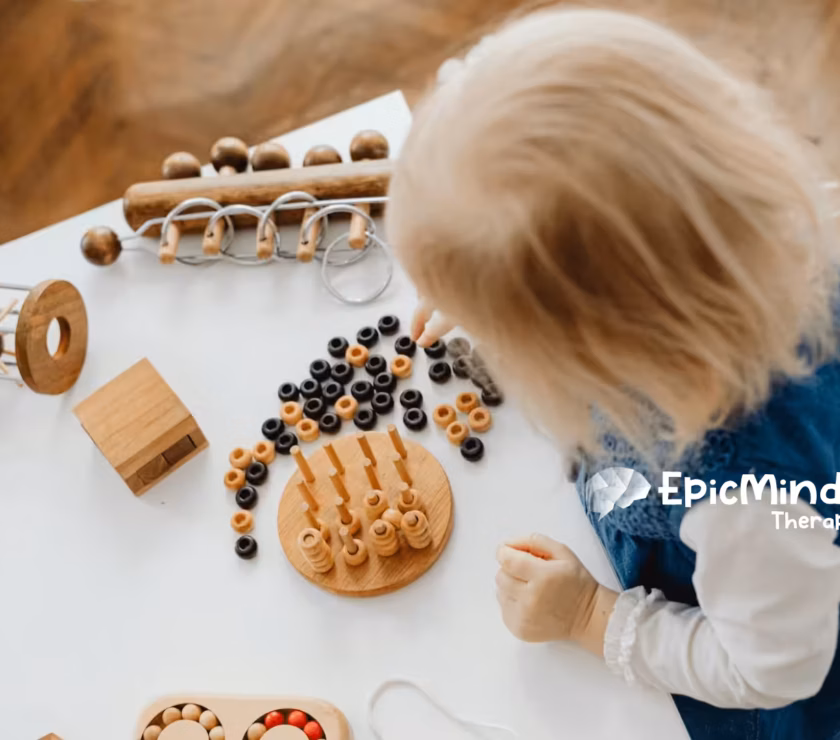 An autistic toddler playing with wooden Montessori toys on a white table during in-home ABA therapy in North Carolina.