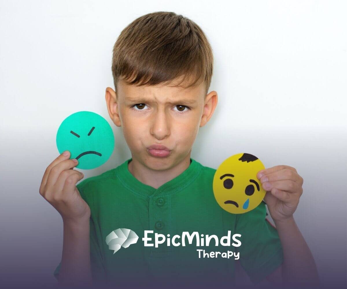A boy with autism holding two large paper emoticons, one sad and one crying.