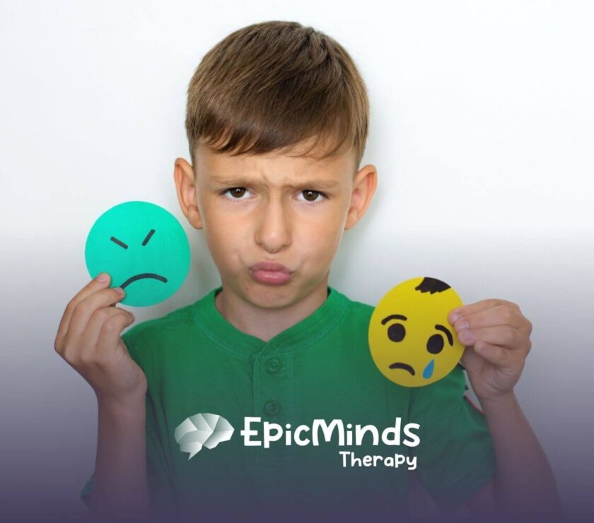 A boy with autism holding two large paper emoticons, one sad and one crying.