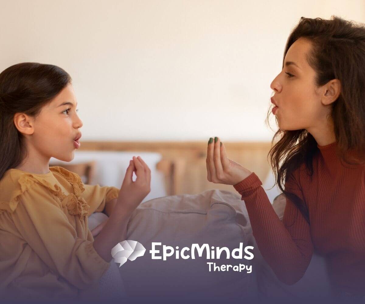 An ABA therapist and autistic girl sitting together, playing a hand game or pronunciation exercise in ABA therapy.