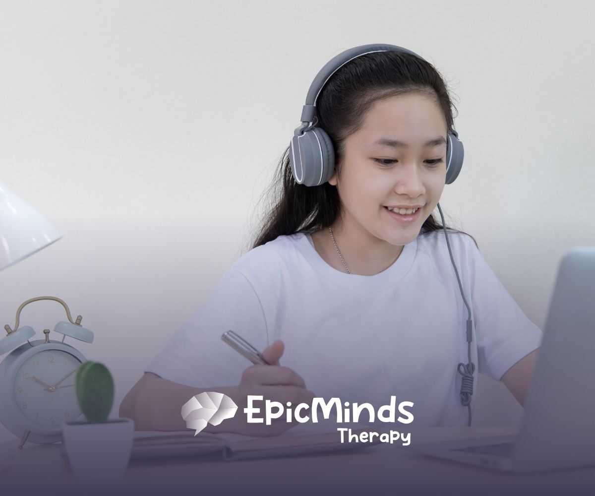 A smiling girl wearing headphones studies at a laptop, writing in a notebook. A desk lamp, alarm clock, and small cactus are beside her, conveying focus.