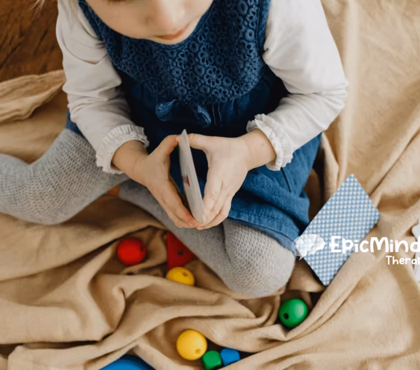 An autistic toddler sitting on a blanket playing with flashcards and colorful toys during ABA therapy in NC.