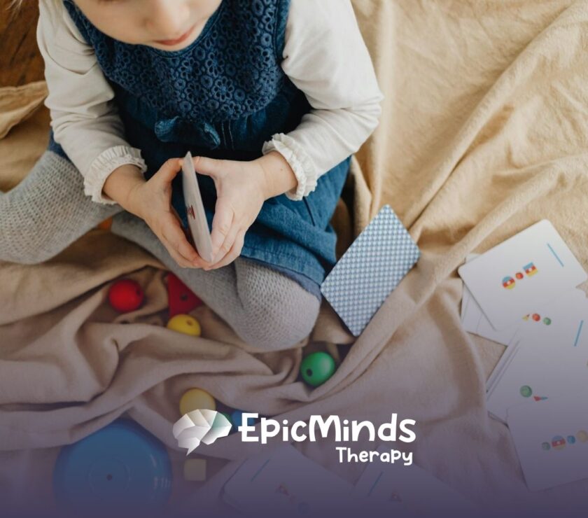 An autistic toddler sitting on a blanket playing with flashcards and colorful toys during ABA therapy in NC.