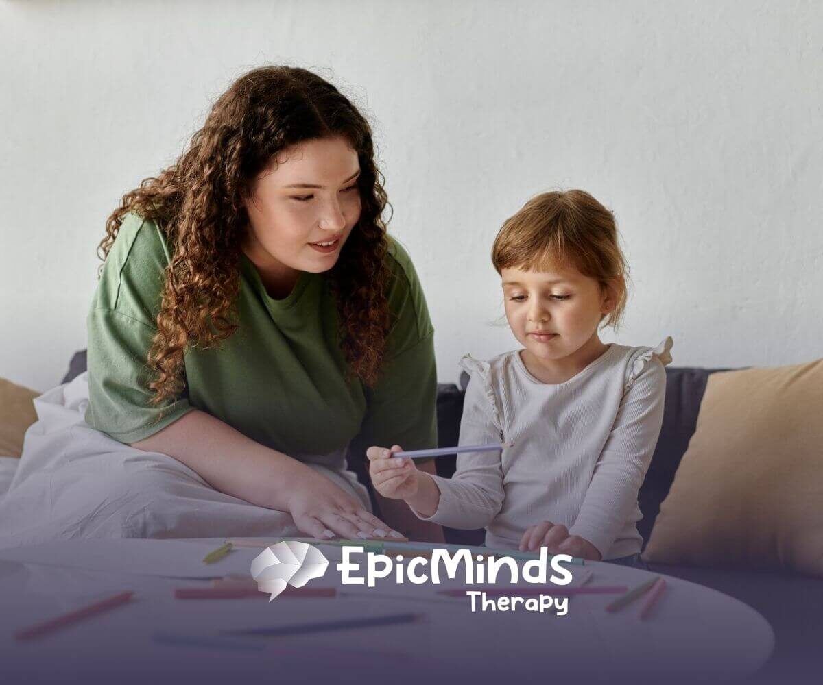 A girl with autism choosing a colored pencil while sitting at a table with an ABA therapist.