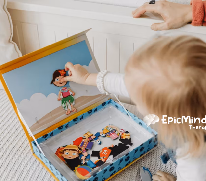 An autistic toddler playing with a magnetic dress-up doll set on a bed during in-home ABA therapy in North Carolina.