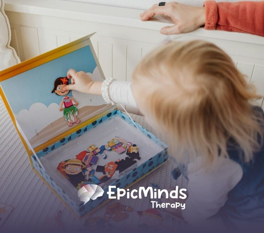 An autistic toddler playing with a magnetic dress-up doll set on a bed during in-home ABA therapy in North Carolina.