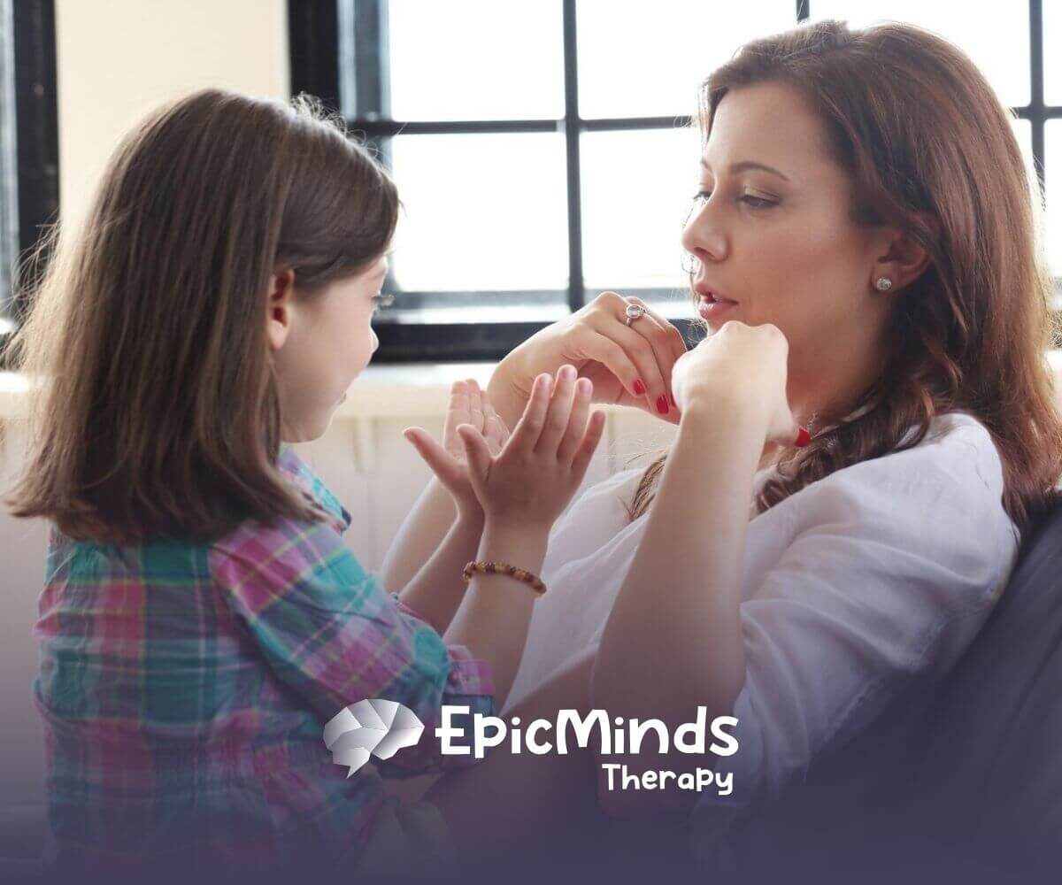 A child with autism and an ABA therapist sitting together and playing hand games in ABA therapy.