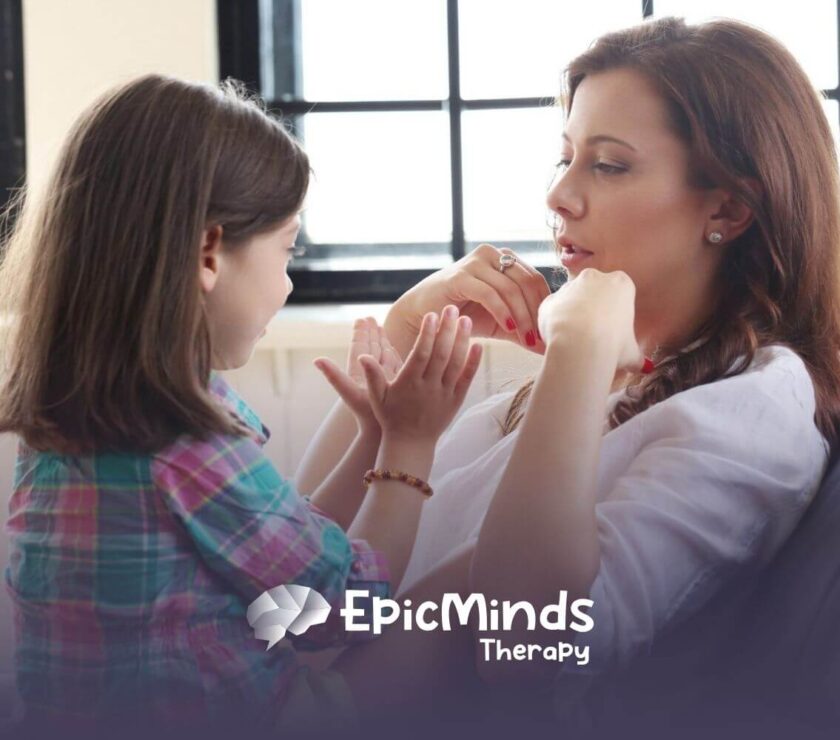 A child with autism and an ABA therapist sitting together and playing hand games in ABA therapy.