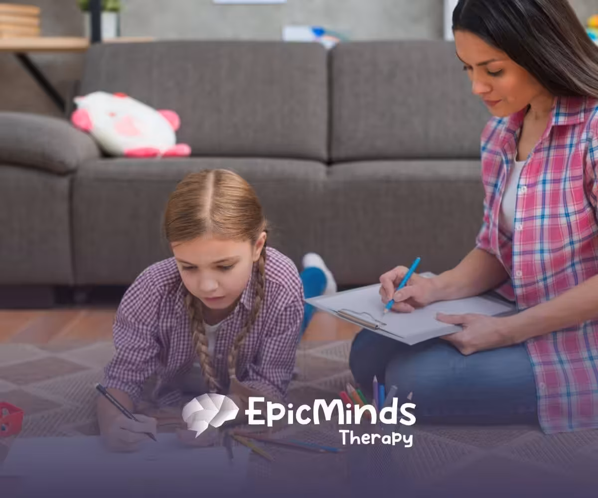 Autistic girl drawing on paper on the floor while ABA therapist beside her takes notes during ABA therapy.