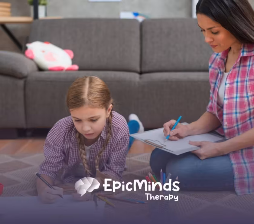 Autistic girl drawing on paper on the floor while ABA therapist beside her takes notes during ABA therapy.