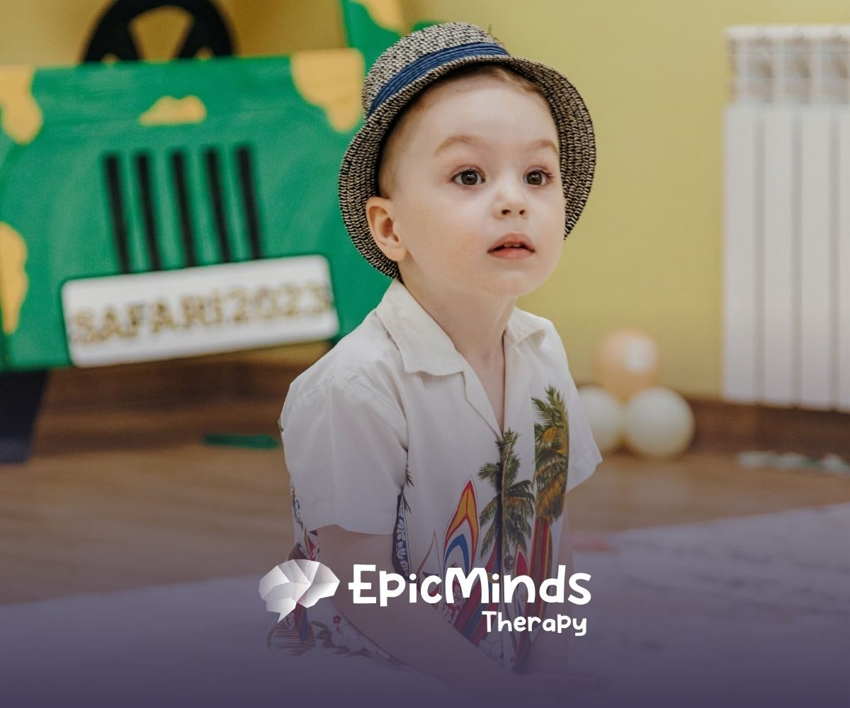 A young child with a curious expression wears a patterned hat and a white shirt with palm leaves. Behind, a safari-themed backdrop and soft lighting set a playful tone.