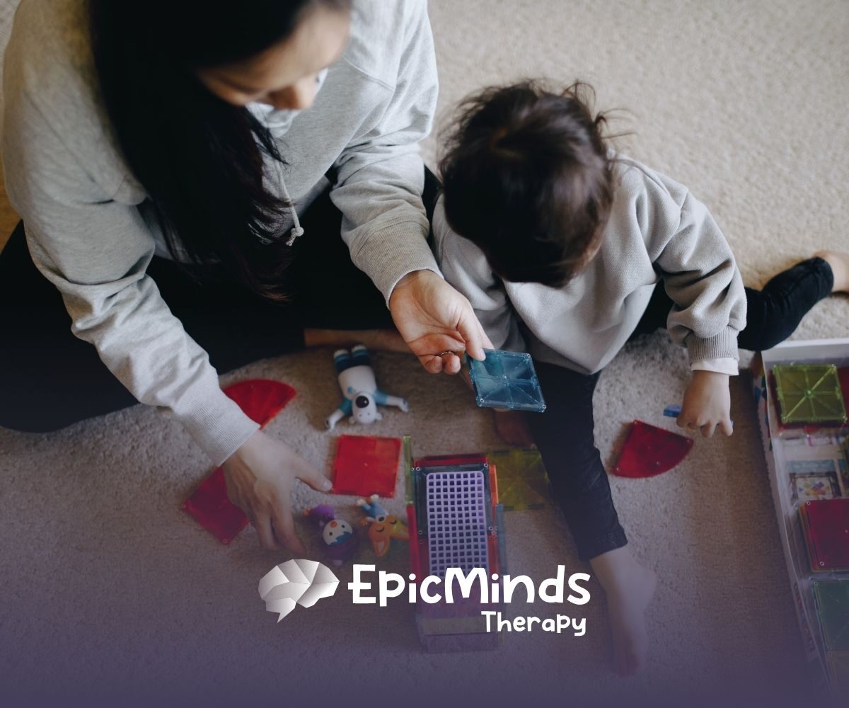 A caregiver and child play with colorful magnetic tiles on a carpet. The scene is cozy and engaging, suggesting learning and creativity.