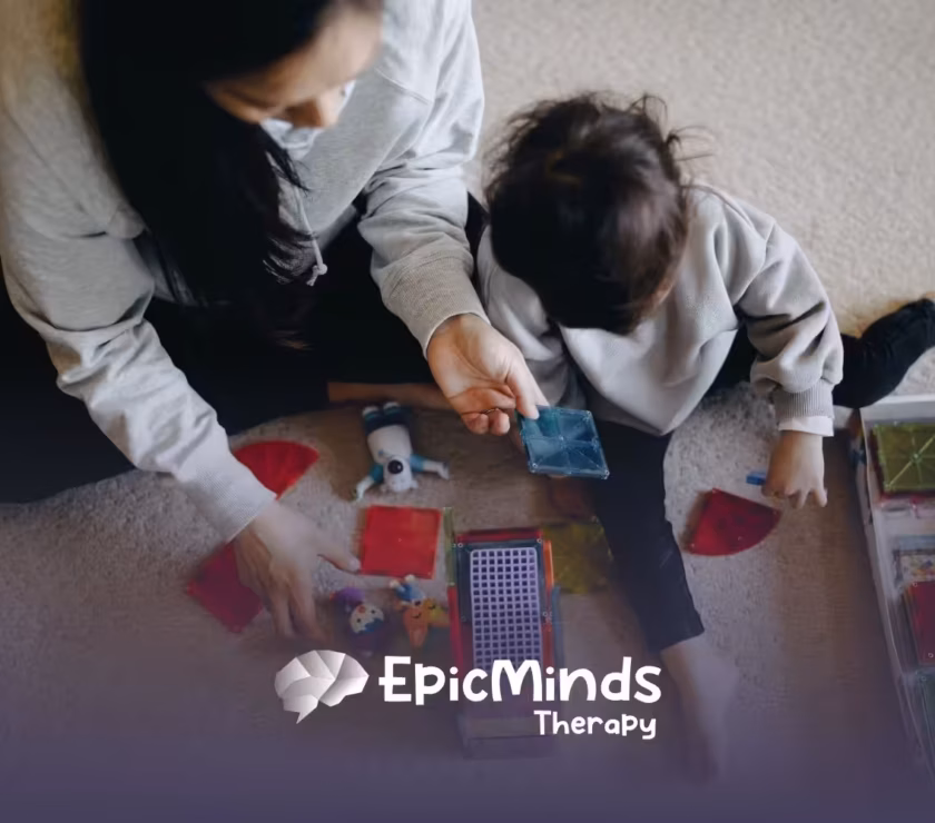 A caregiver and child play with colorful magnetic tiles on a carpet. The scene is cozy and engaging, suggesting learning and creativity.