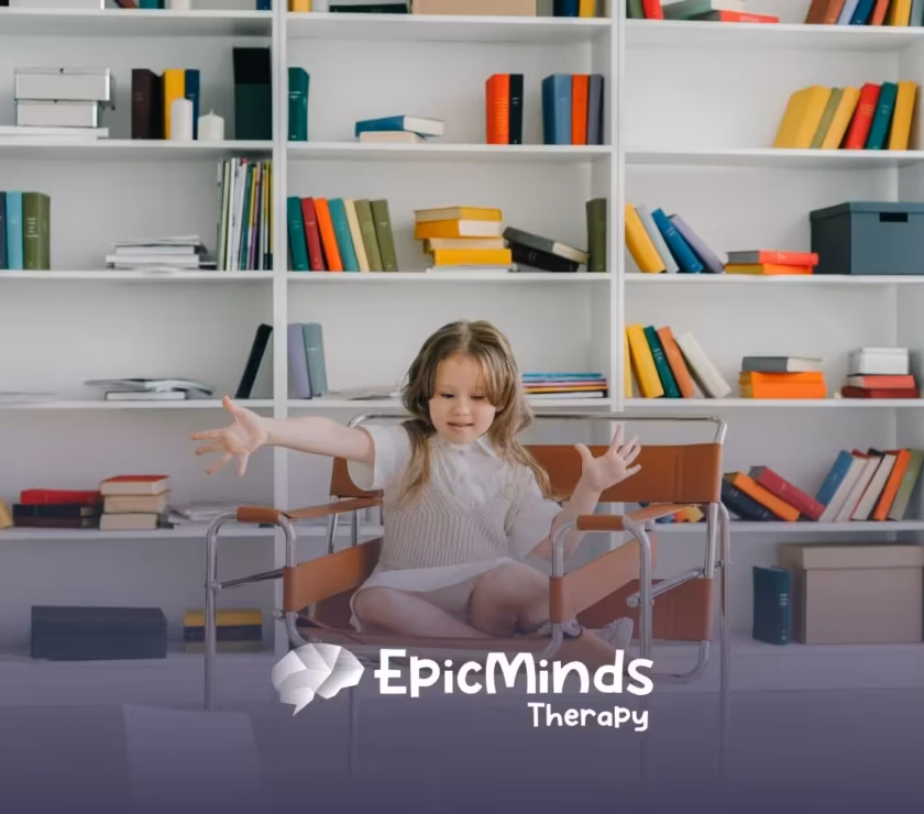 A young girl sits cross-legged on a brown chair in a library, reaching out with an engaged expression. Shelves behind her are filled with colorful books.