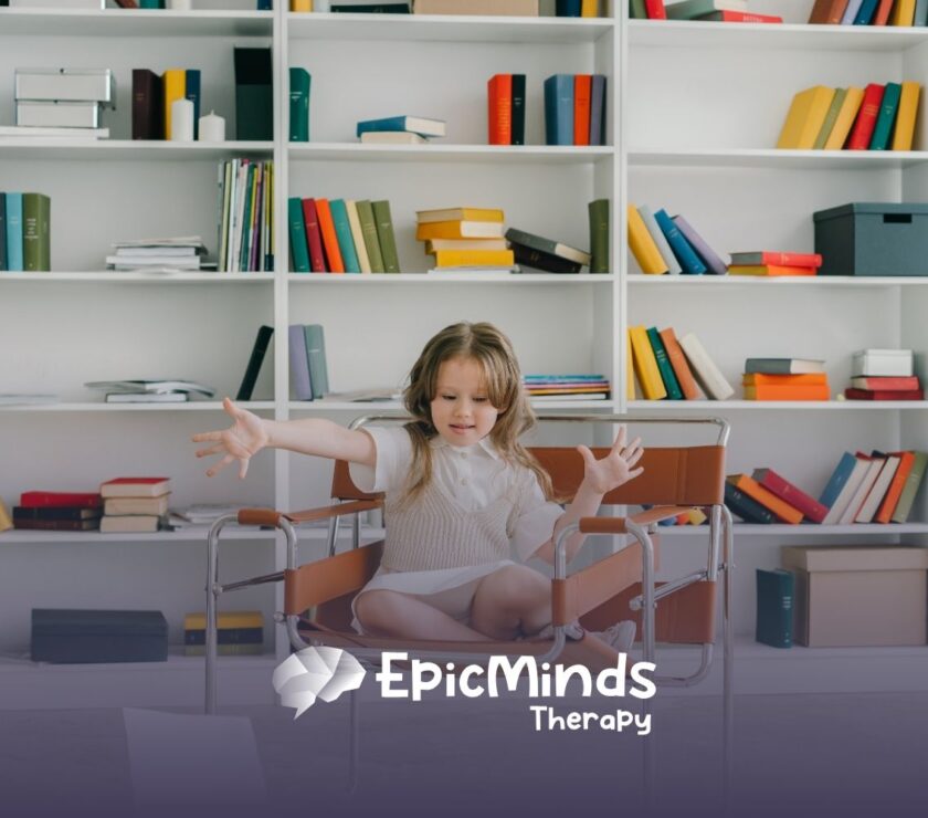 A young girl sits cross-legged on a brown chair in a library, reaching out with an engaged expression. Shelves behind her are filled with colorful books.