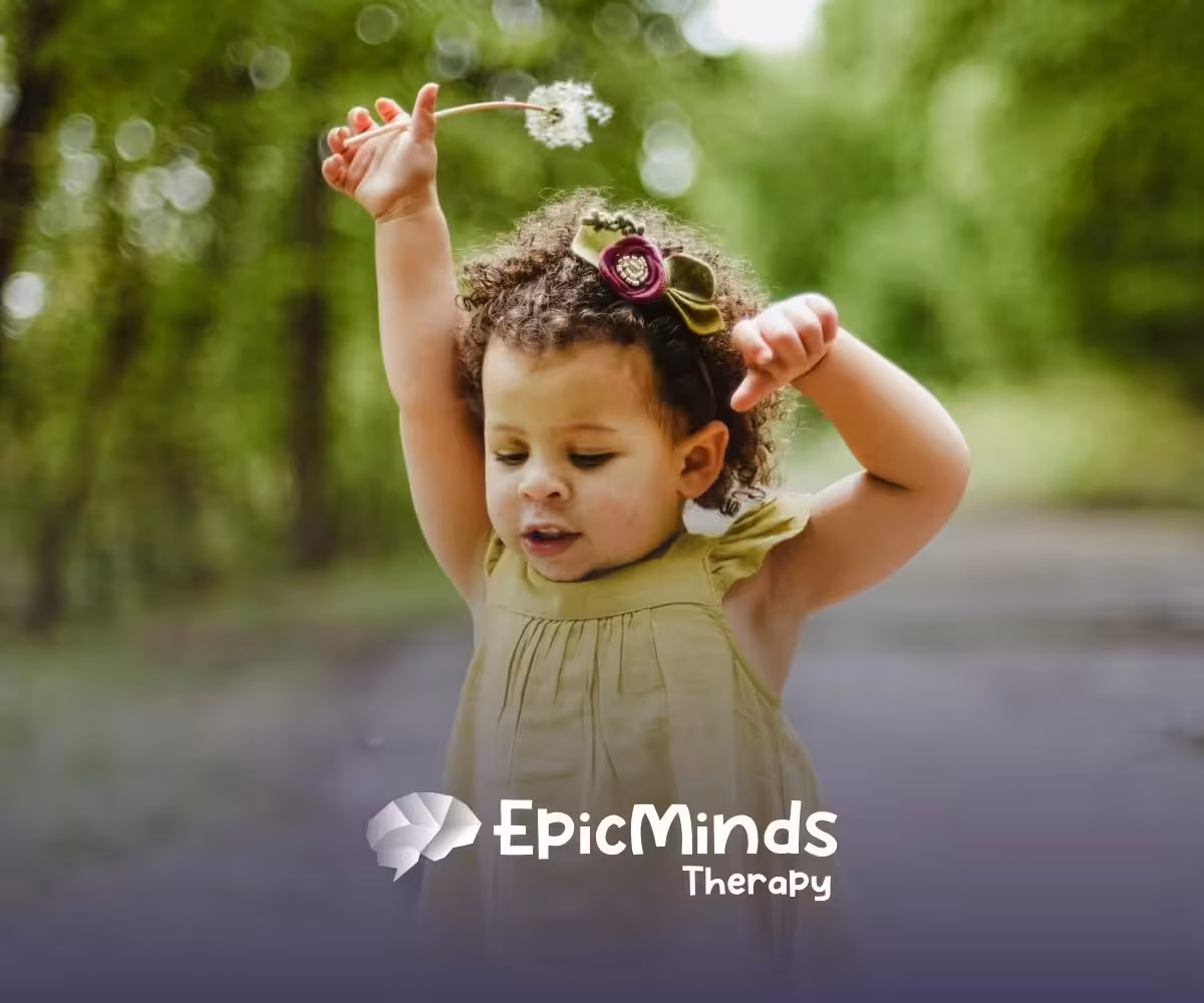 Young autistic girl playing with a dandelion in a green outdoor area, enjoying nature during ABA therapy in NC.