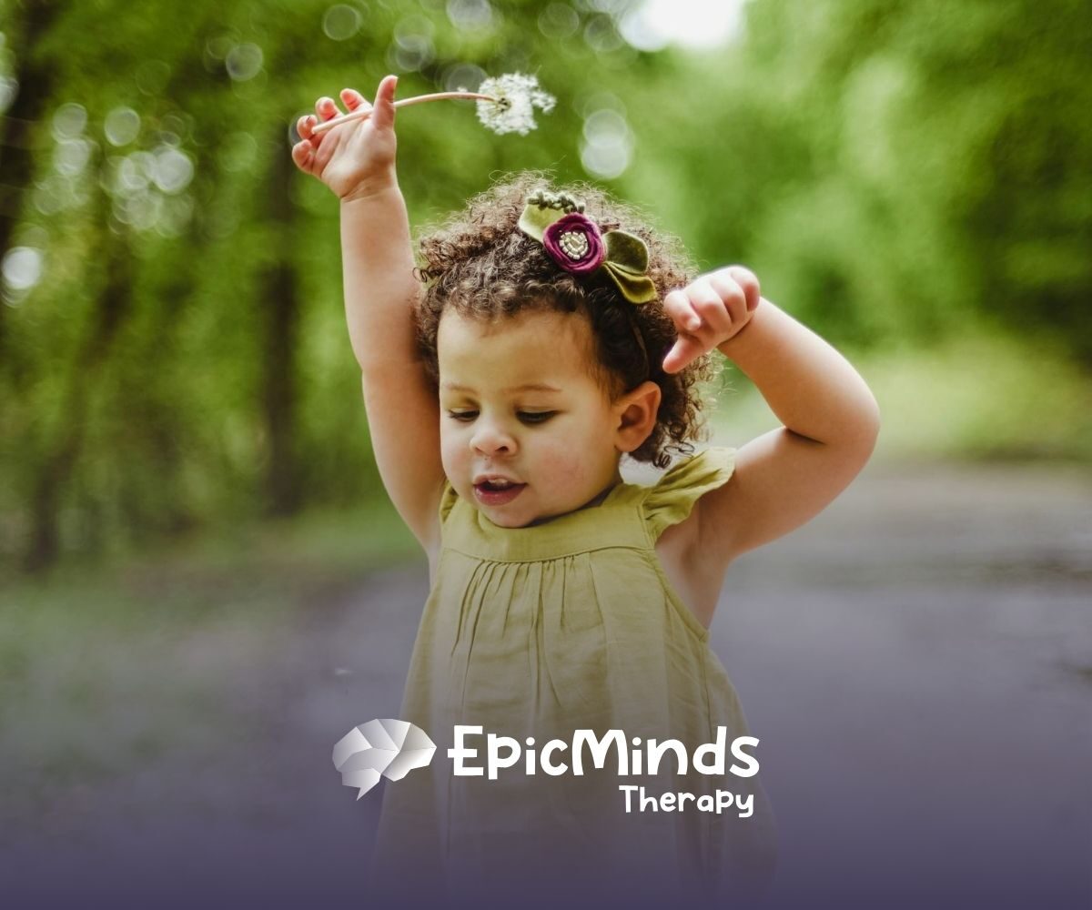 Young autistic girl playing with a dandelion in a green outdoor area, enjoying nature during ABA therapy in NC.