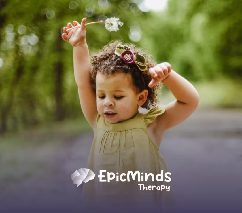 Young autistic girl playing with a dandelion in a green outdoor area, enjoying nature during ABA therapy in NC.