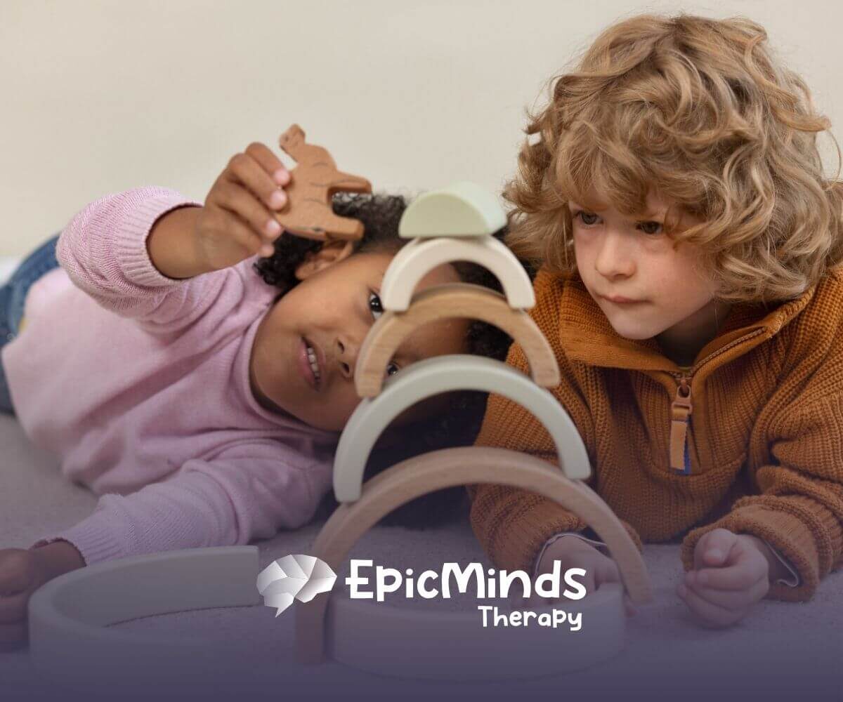 Two young children with autism lay on the floor, focused on stacking wooden arches in ABA therapy.
