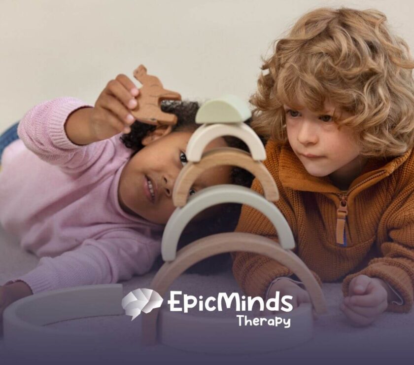 Two young children with autism lay on the floor, focused on stacking wooden arches in ABA therapy.