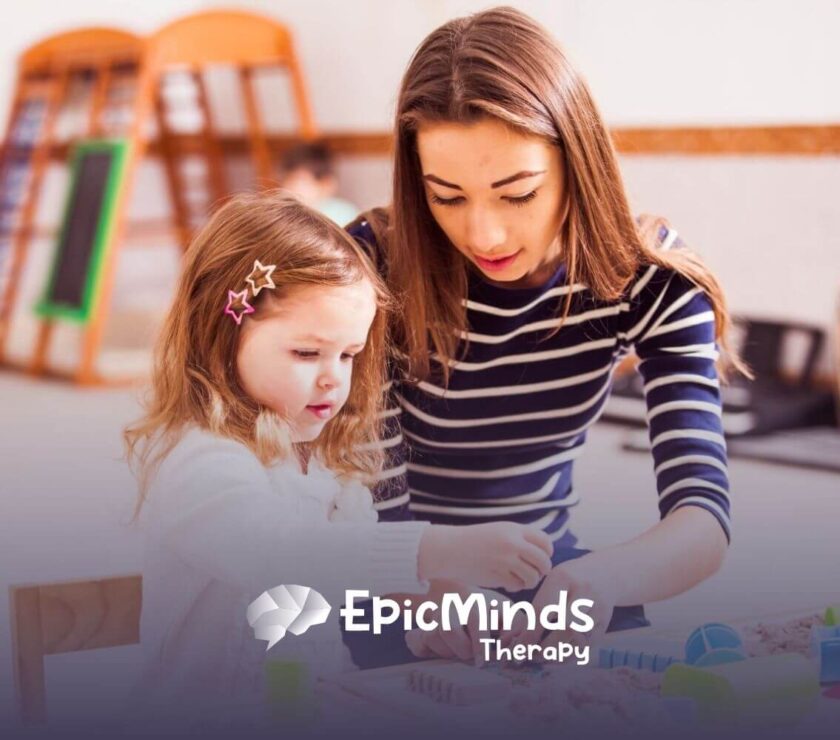 An ABA therapist helps a little girl play with kinetic sand and toys at a table in ABA therapy.