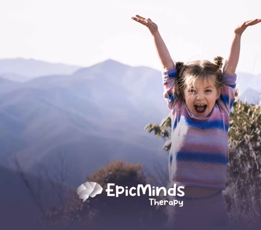Young girl with pigtails, wearing a colorful sweater, joyfully raises her arms against a backdrop of misty mountains and foliage.
