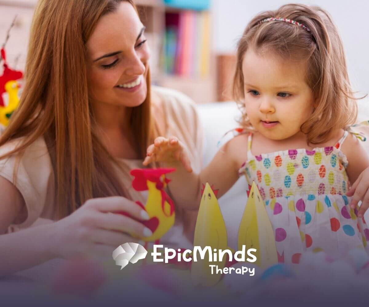 An ABA therapist and a toddler play with colorful paper crafts shaped like chickens in ABA therapy.