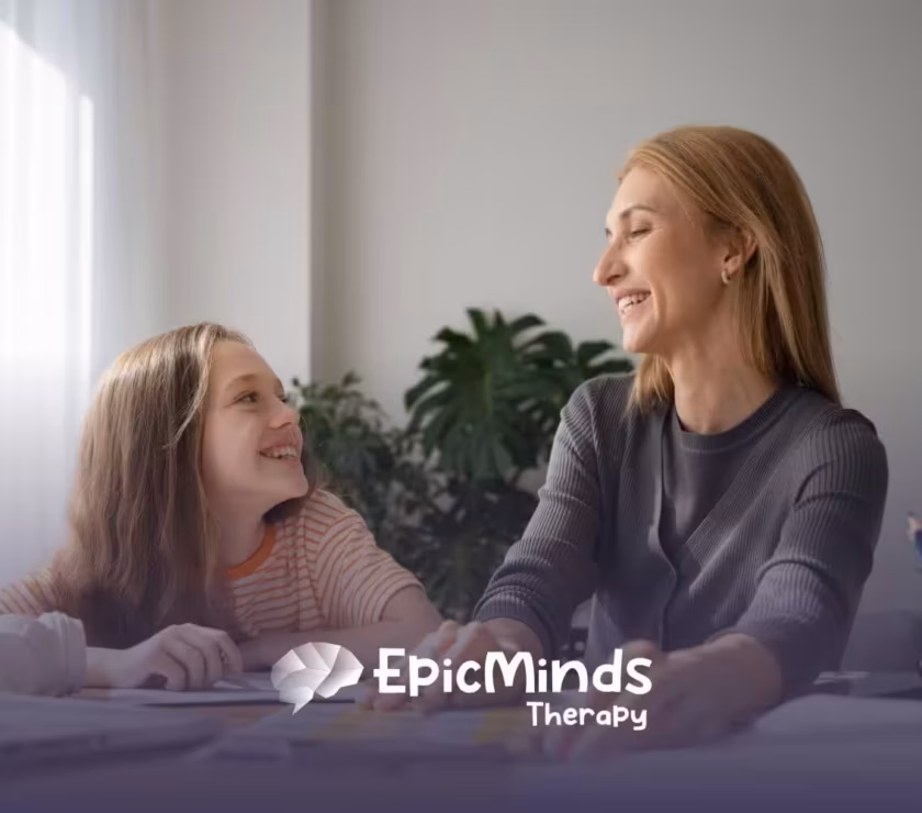 An ABA therapist and autistic girl smile at each other while doing an activity in ABA therapy.