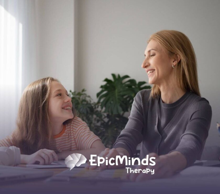 An ABA therapist and autistic girl smile at each other while doing an activity in ABA therapy.