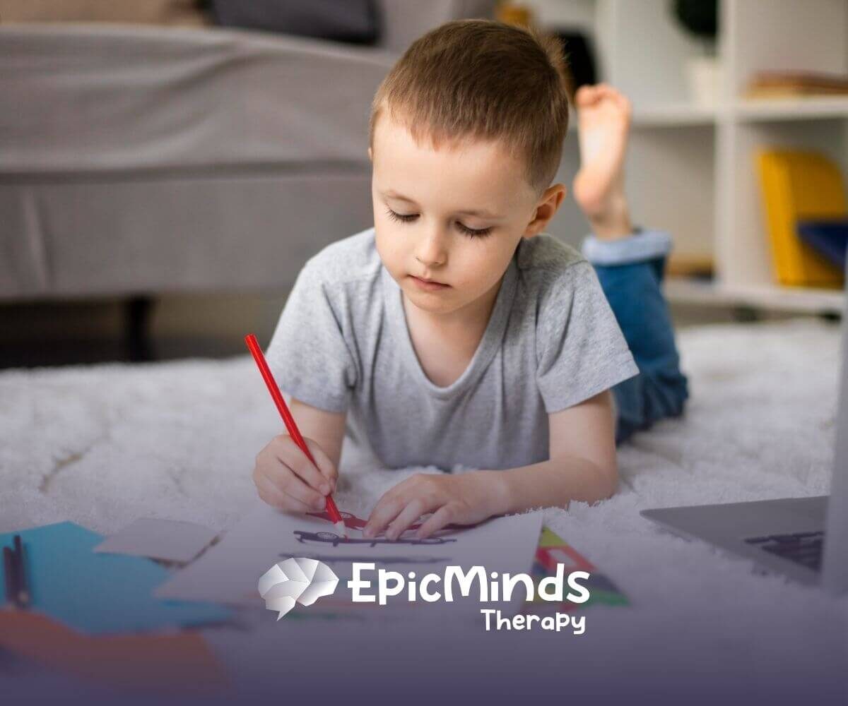 A boy with autism lies on the floor, drawing with a red pencil in ABA therapy.