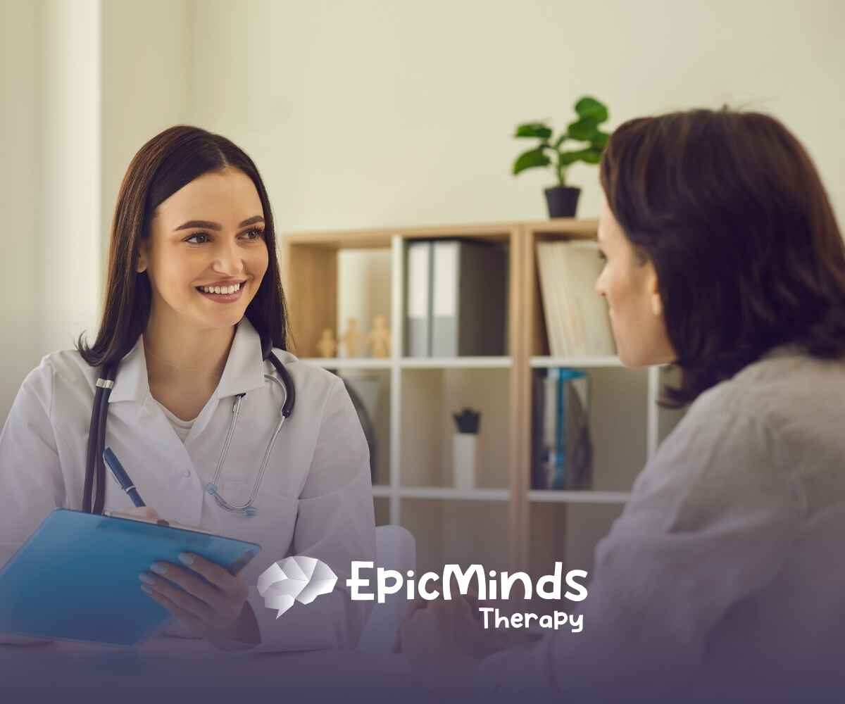 A smiling doctor with long dark hair holds a clipboard, attentively speaking to a patient in a well-lit office